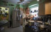 A woman stands in front of a stove tending to a boiling pot. 