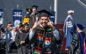 A student wearing a robe and mortarboard celebrates.